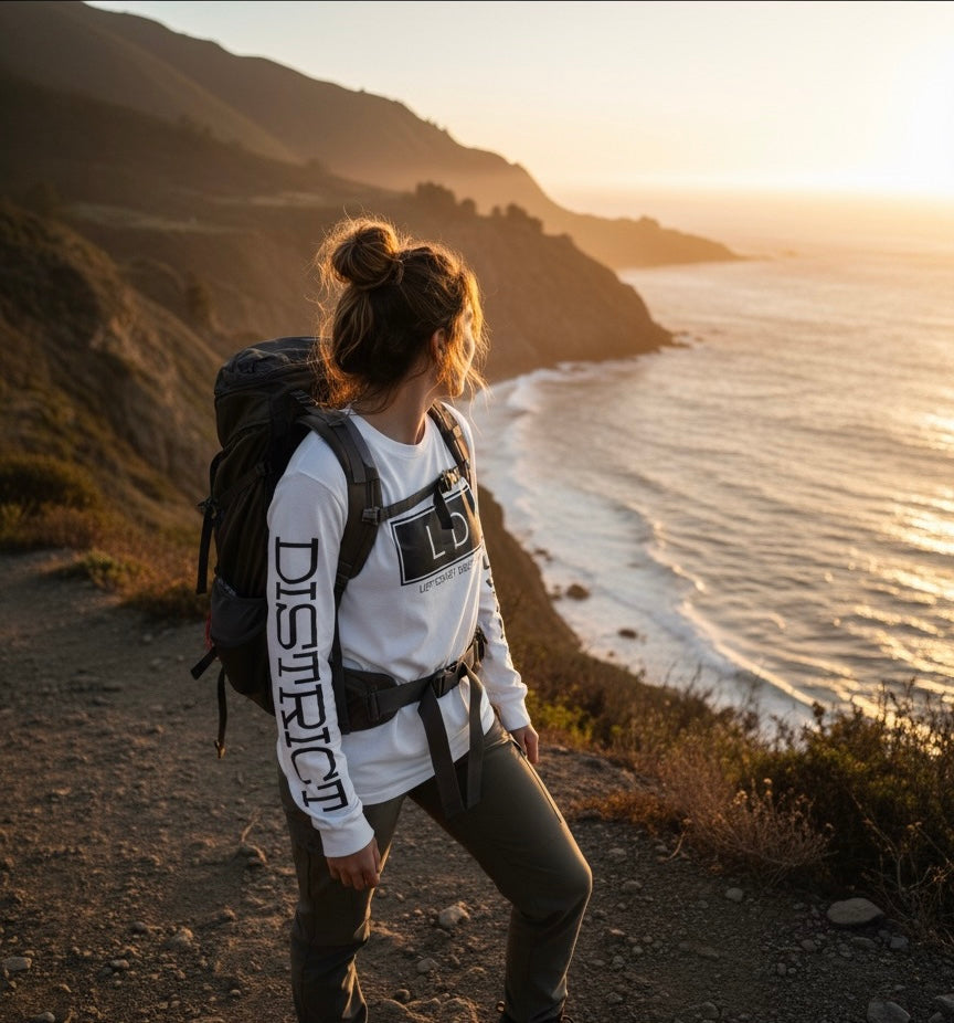 Person with a backpack standing on a coastal trail at sunset